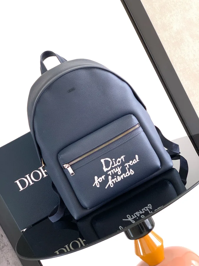 Mochila Dior azul-marinho com alças duplas e bolso frontal fotografada sobre caixa, foto do álbum