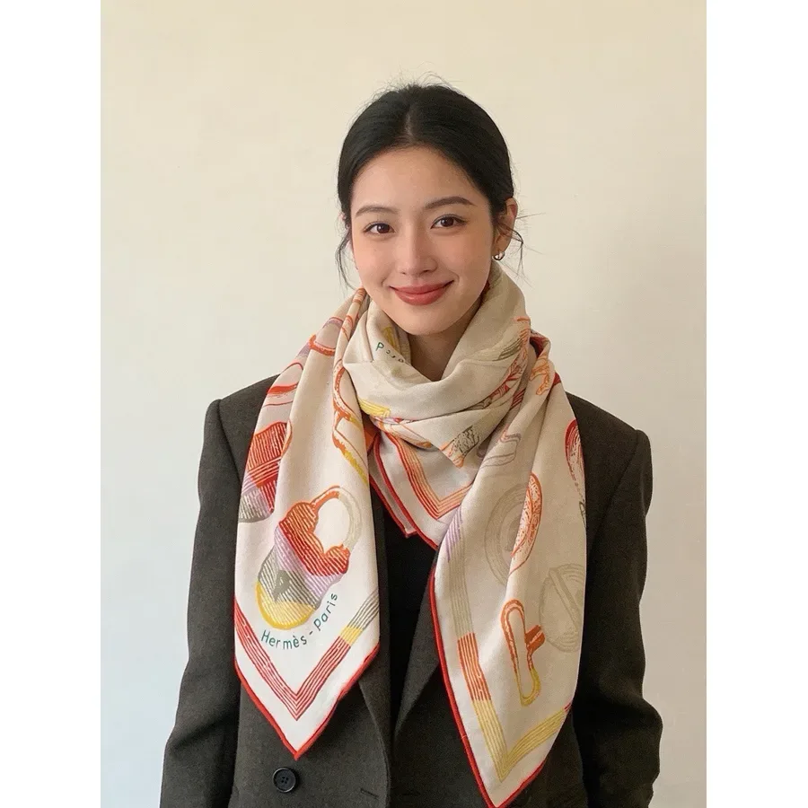 Cream square silk scarf with an orange, red and yellow chain-link and padlock print, draped around the neck over a dark blazer