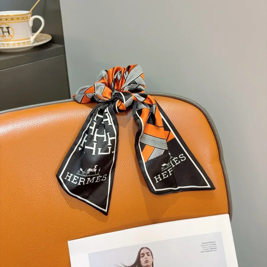 Silk ribbon with a black, orange and white carriage print tied around the handle of a tan leather bag