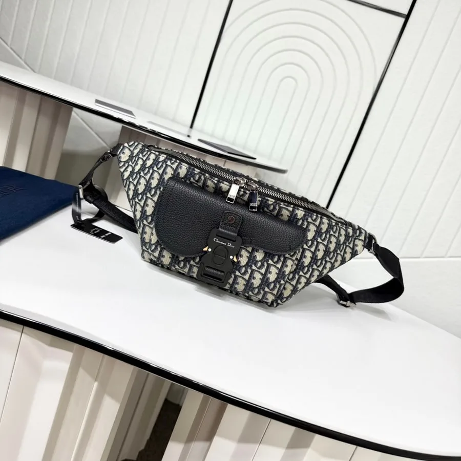 Grey and white Dior Oblique jacquard Saddle bag with a black leather flap and a long black strap, photographed on a white counter