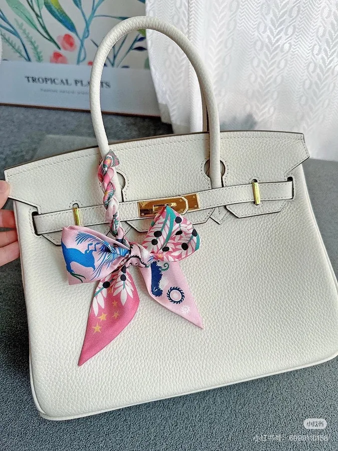 Off-white pebbled leather top-handle bag with two rolled handles, front straps with gold tips and a gold turn-lock plate, from the GunongTrade catalog