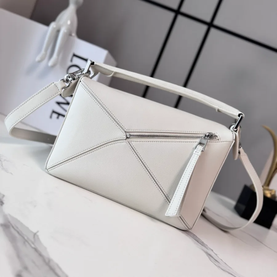 White LOEWE Puzzle-style bag photographed from the front, showing triangular panel seams, a top zip with a leather pull and a detachable strap