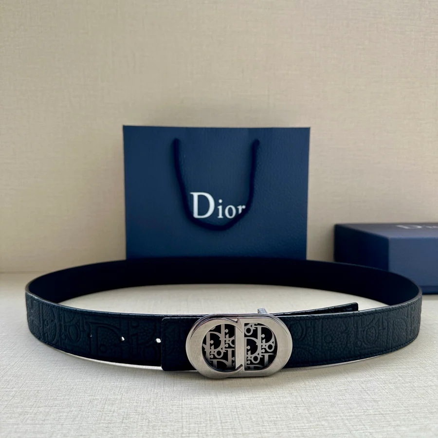 Black leather Dior belt photographed coiled on a pale surface, buckle and strap end both visible