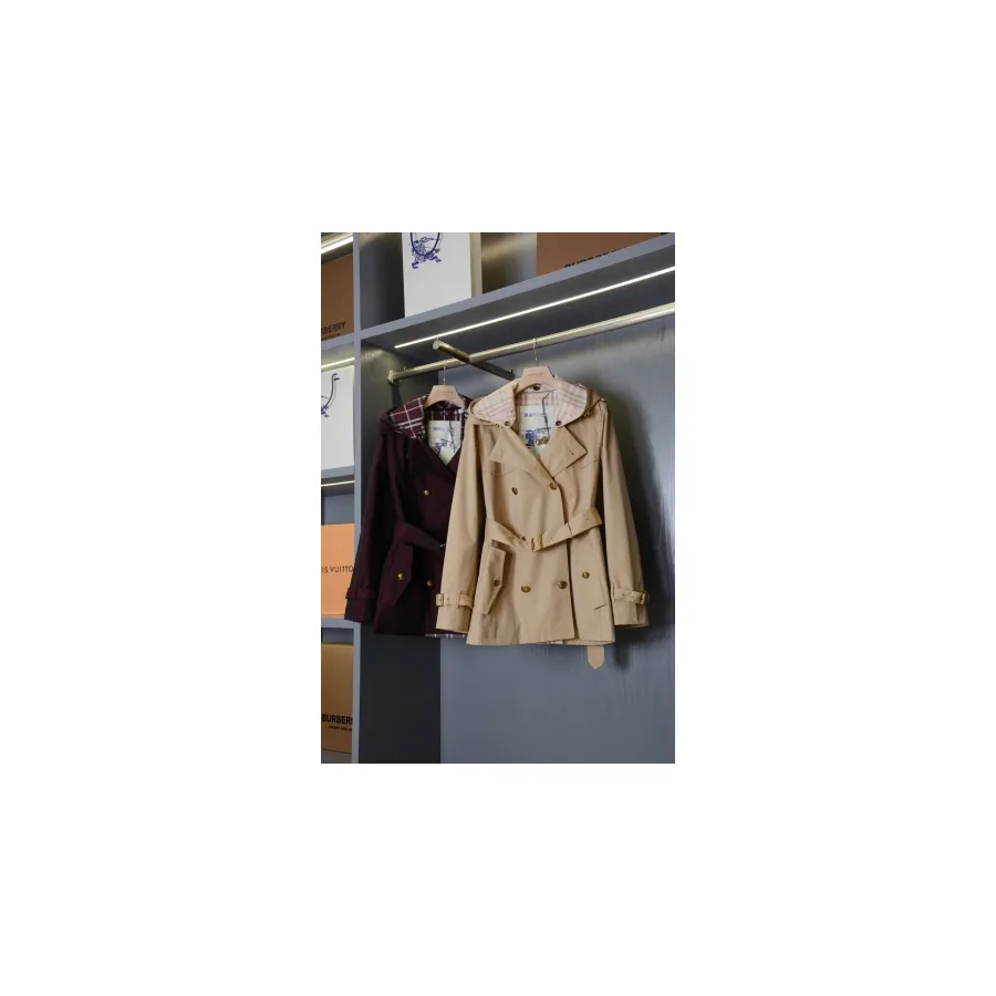 Short beige Burberry trench coat on a hanger showing belted cuffs, a storm flap and a check lining