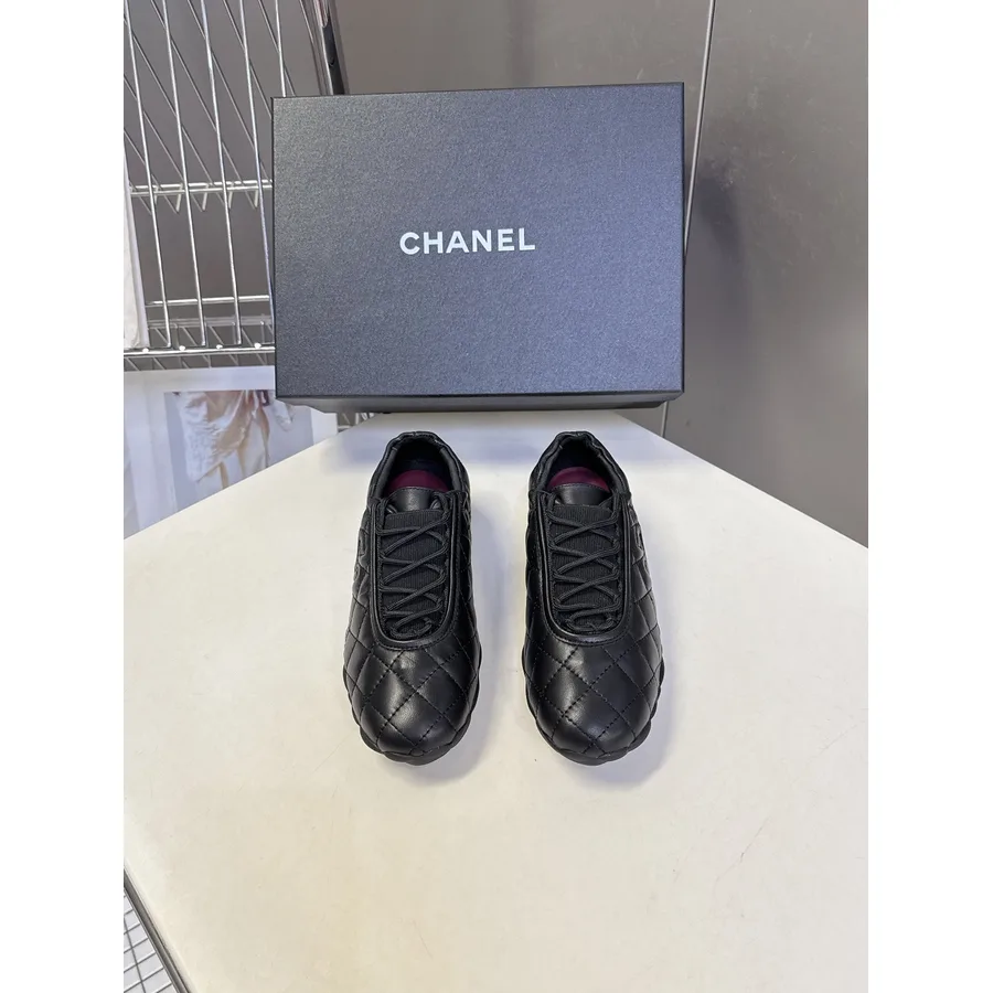 All-black low-top Chanel sneaker with a quilted diamond-stitched leather toe box and side panels, black laces and a small interlocking CC logo near the heel