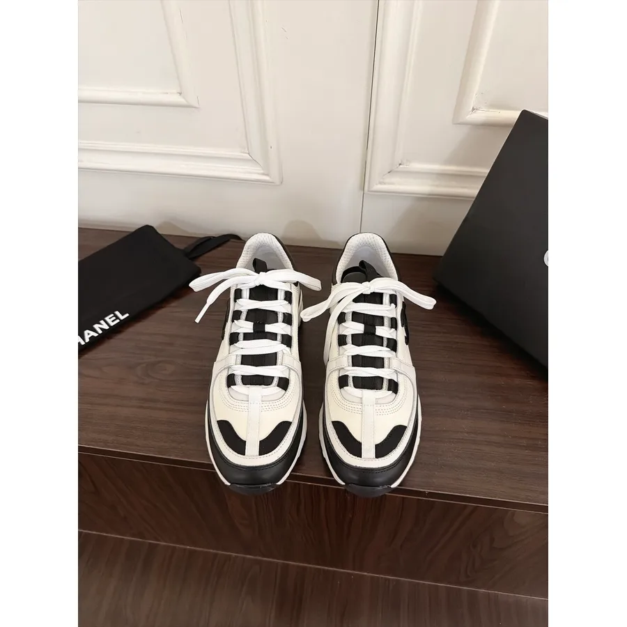 Black and white Chanel sneaker with a white mesh base, white leather overlays, black suede panels across the toe and side, white crisscross laces and a medium-thick black and white sole