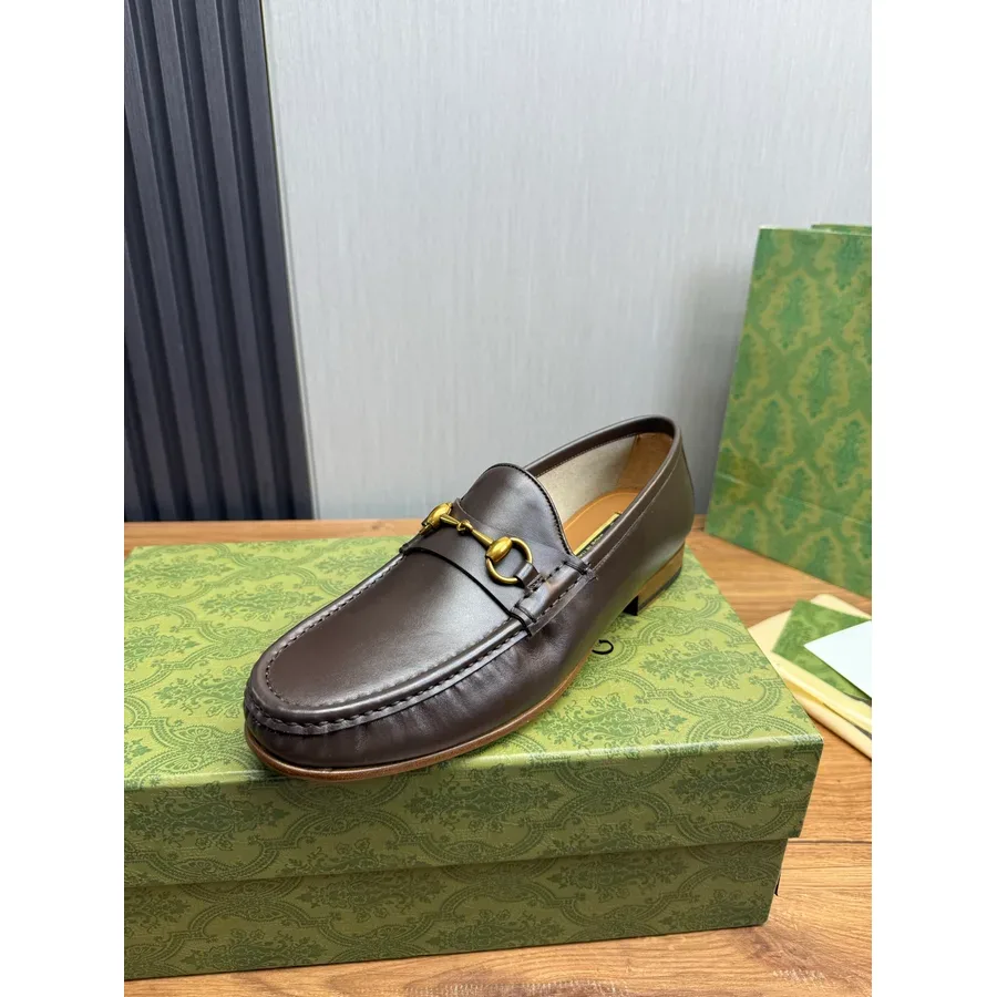 Brown leather loafer with a gold horsebit across the vamp, photographed on a patterned green box