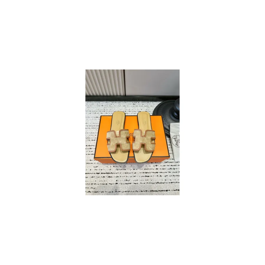 Pair of beige flat slide sandals with an H-shaped cut-out across the strap, photographed in front of an orange box