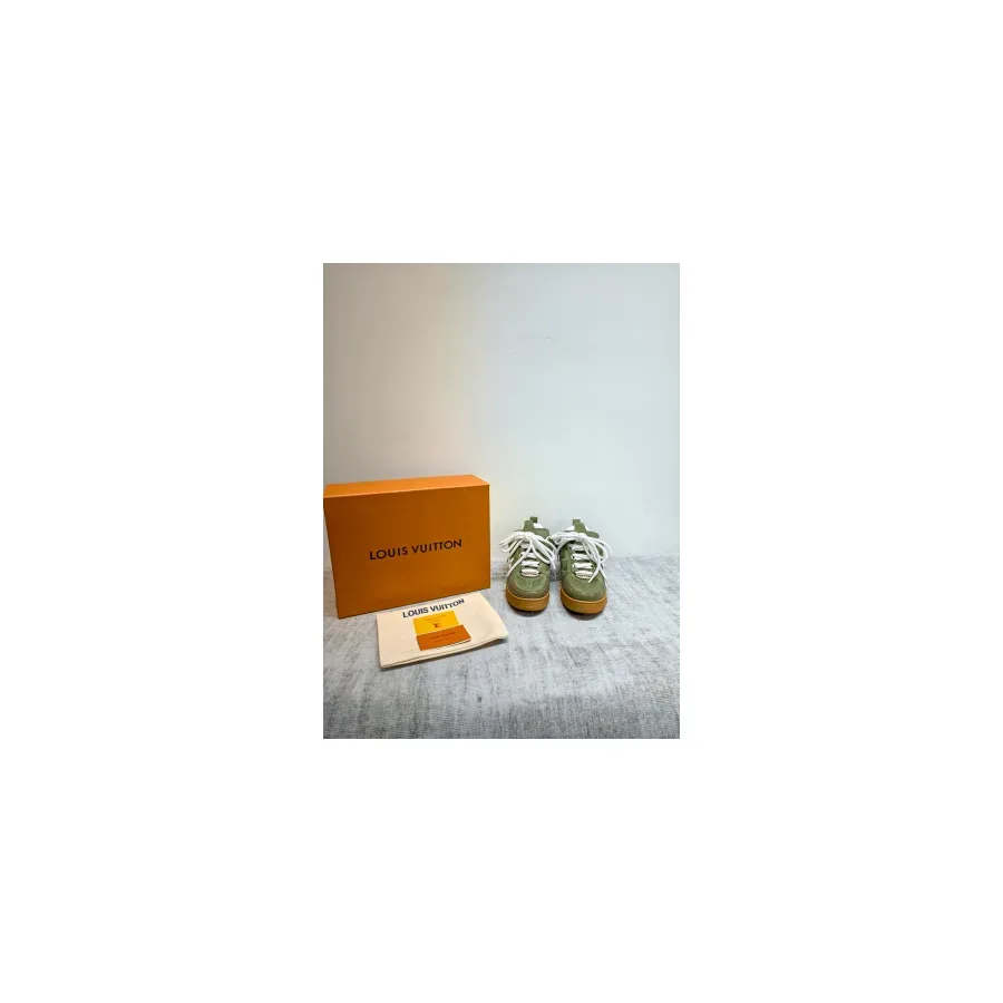 White and green LV Trainer sneakers with white laces, shown next to an orange Louis Vuitton box and a dust bag