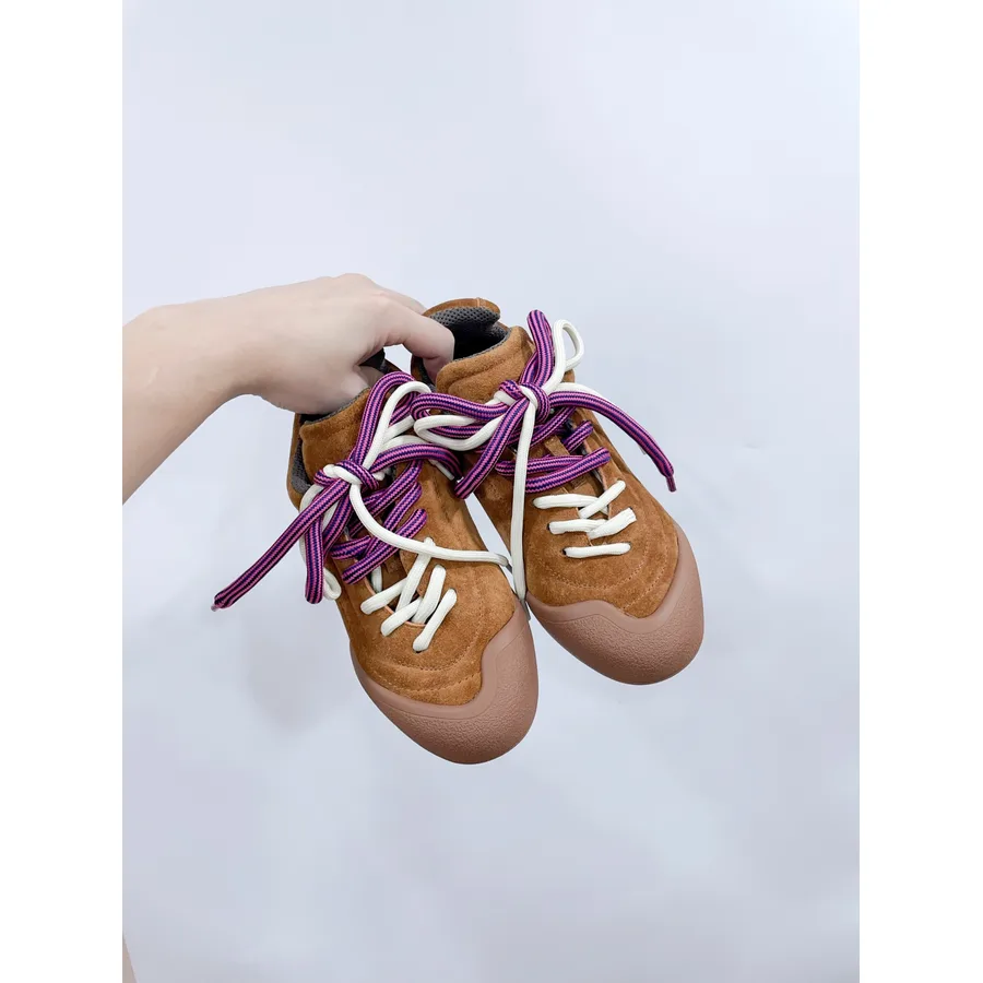 Tan suede McQueen-style low-top held in hand, showing padded collar, smooth toe cap and purple-and-white rope laces