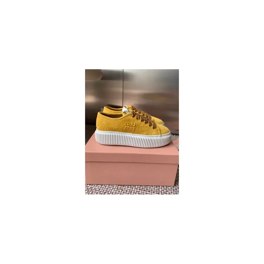 Yellow textured low-top sneaker with brown laces, a white logo tag on the tongue, and a thick white ribbed platform sole with embossing on the side