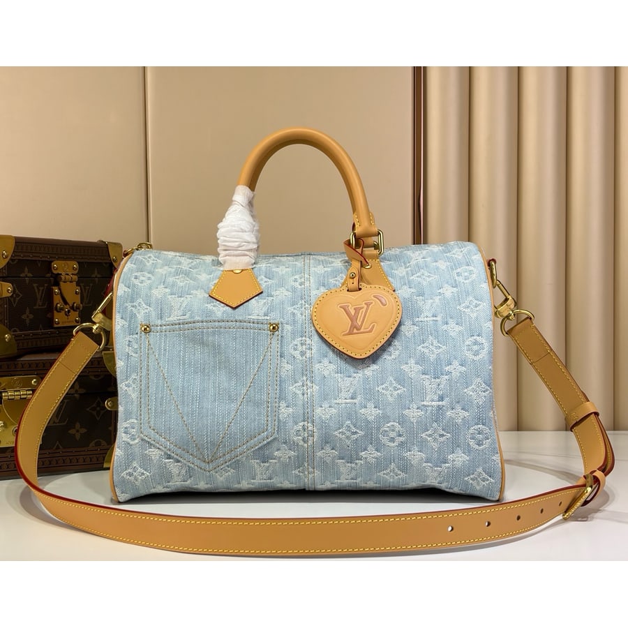 Light blue denim Monogram Speedy Soft 30 with a front slip pocket and tan strap, shown beside a trunk on a white table