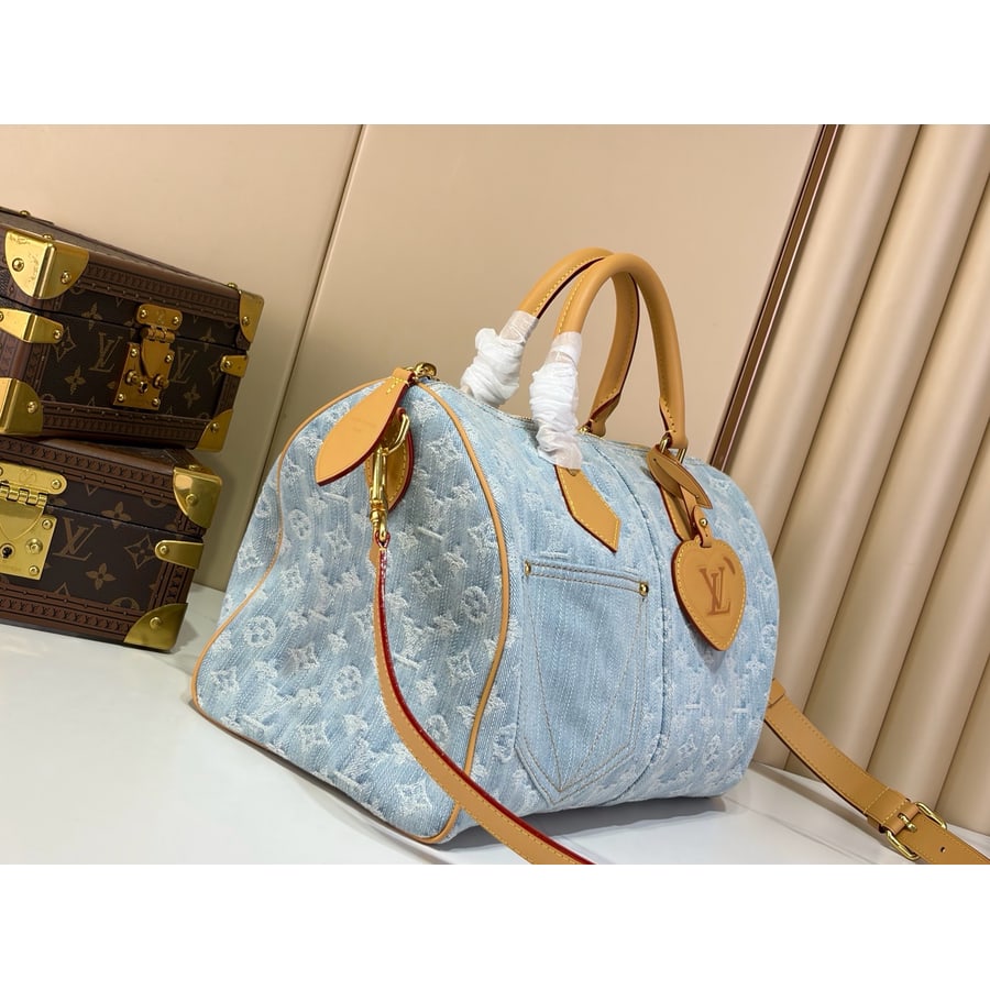 The light blue denim Speedy Soft 30 from the front with the tan strap hung on one side and a heart-shaped leather tag at the handle